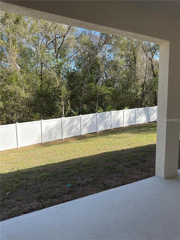 A concrete patio overlooks a grassy backyard enclosed by a white vinyl privacy fence — 8925 N GOLFVIEW DRIVE, CITRUS SPRINGS, FL