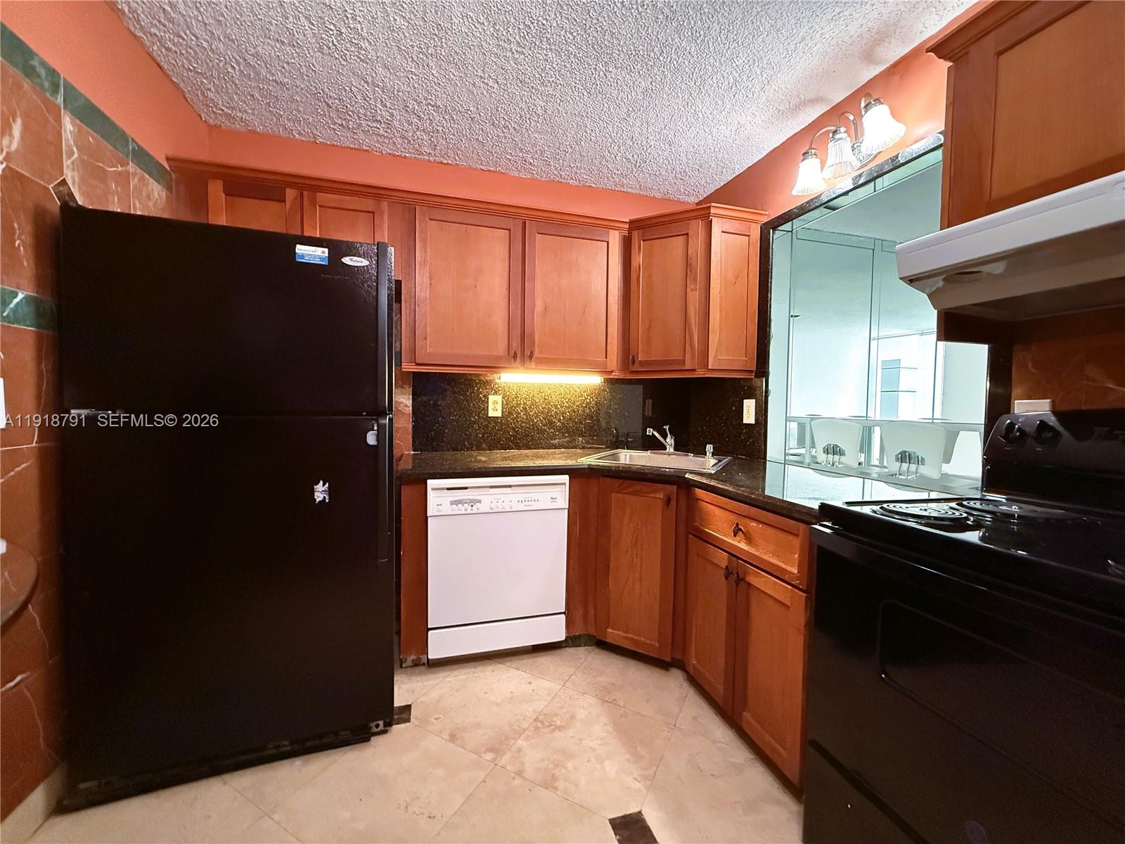 A kitchen features wood cabinets, black appliances, a white dishwasher, and dark granite countertops — 701 Three Islands Blvd # 506, Hallandale Beach FL 33009, HALLANDALE BEACH, FL