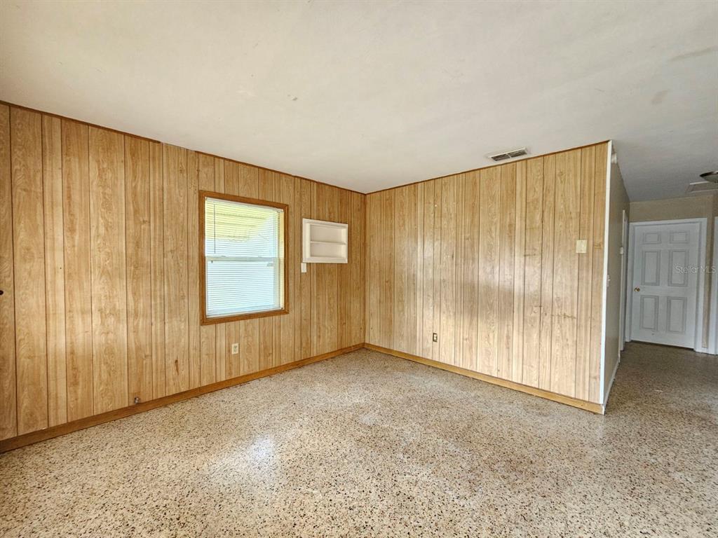 An empty room features wood-paneled walls, a window, and a speckled terrazzo floor — 1216 E MYRTLE STREET, LAKELAND, FL