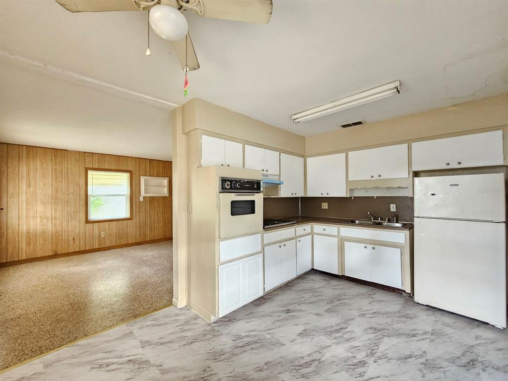 A kitchen with white cabinets, a wall oven, and a refrigerator opens to a living area — 1216 E MYRTLE STREET, LAKELAND, FL