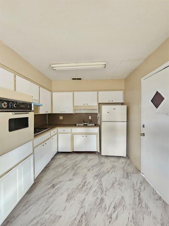 A kitchen features white cabinets, a wall oven, a refrigerator, and marble-patterned vinyl flooring — 1216 E MYRTLE STREET, LAKELAND, FL