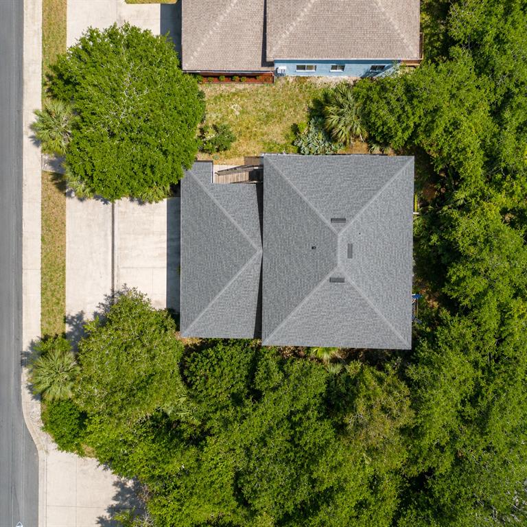 An aerial view shows a house with a gray shingled roof surrounded by dense trees — 601 E 2ND AVENUE, NEW SMYRNA BEACH, FL