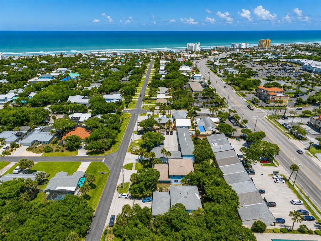 Aerial view of a coastal neighborhood with residential buildings, lush trees, and a nearby beach — 601 E 2ND AVENUE, NEW SMYRNA BEACH, FL
