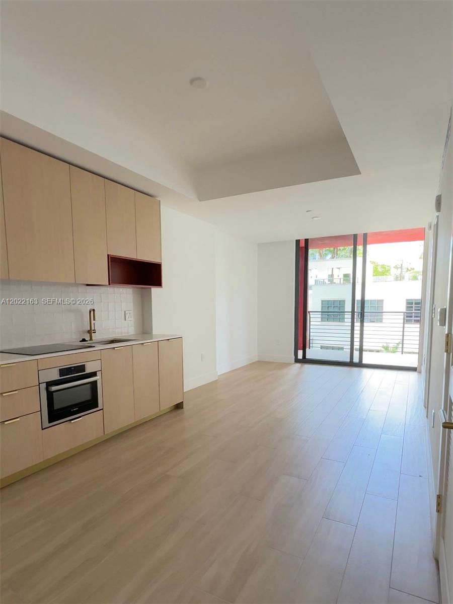 A modern kitchen with light wood cabinets and stainless steel appliances opens to a balcony — 90 NE 32nd St # 510, Miami FL 33145, MIAMI, FL