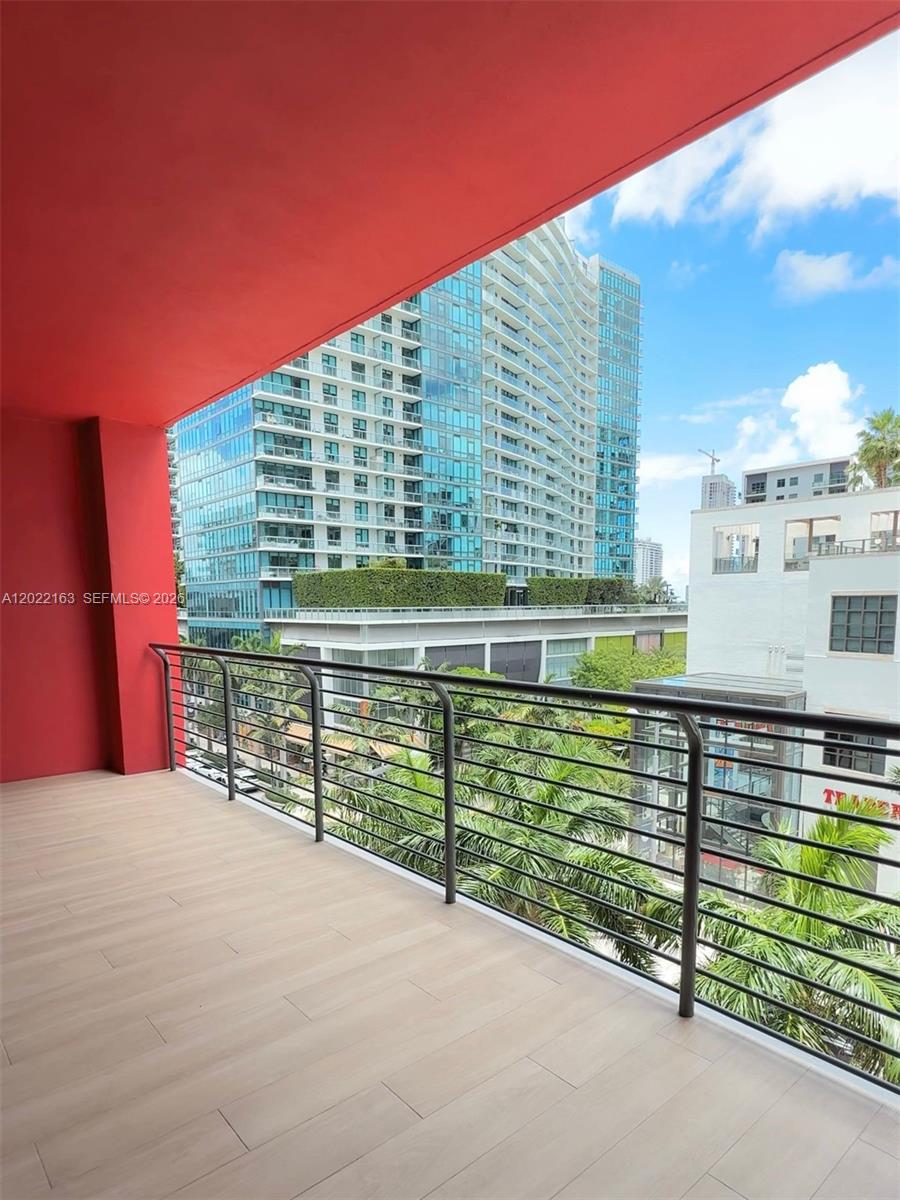 A balcony with light wood-look flooring and a metal railing overlooks a city street — 90 NE 32nd St # 510, Miami FL 33145, MIAMI, FL