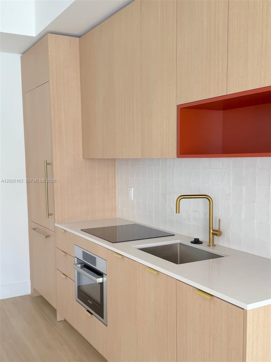 A modern kitchen features light wood cabinets, a white tiled backsplash, and a red accent shelf — 90 NE 32nd St # 510, Miami FL 33145, MIAMI, FL