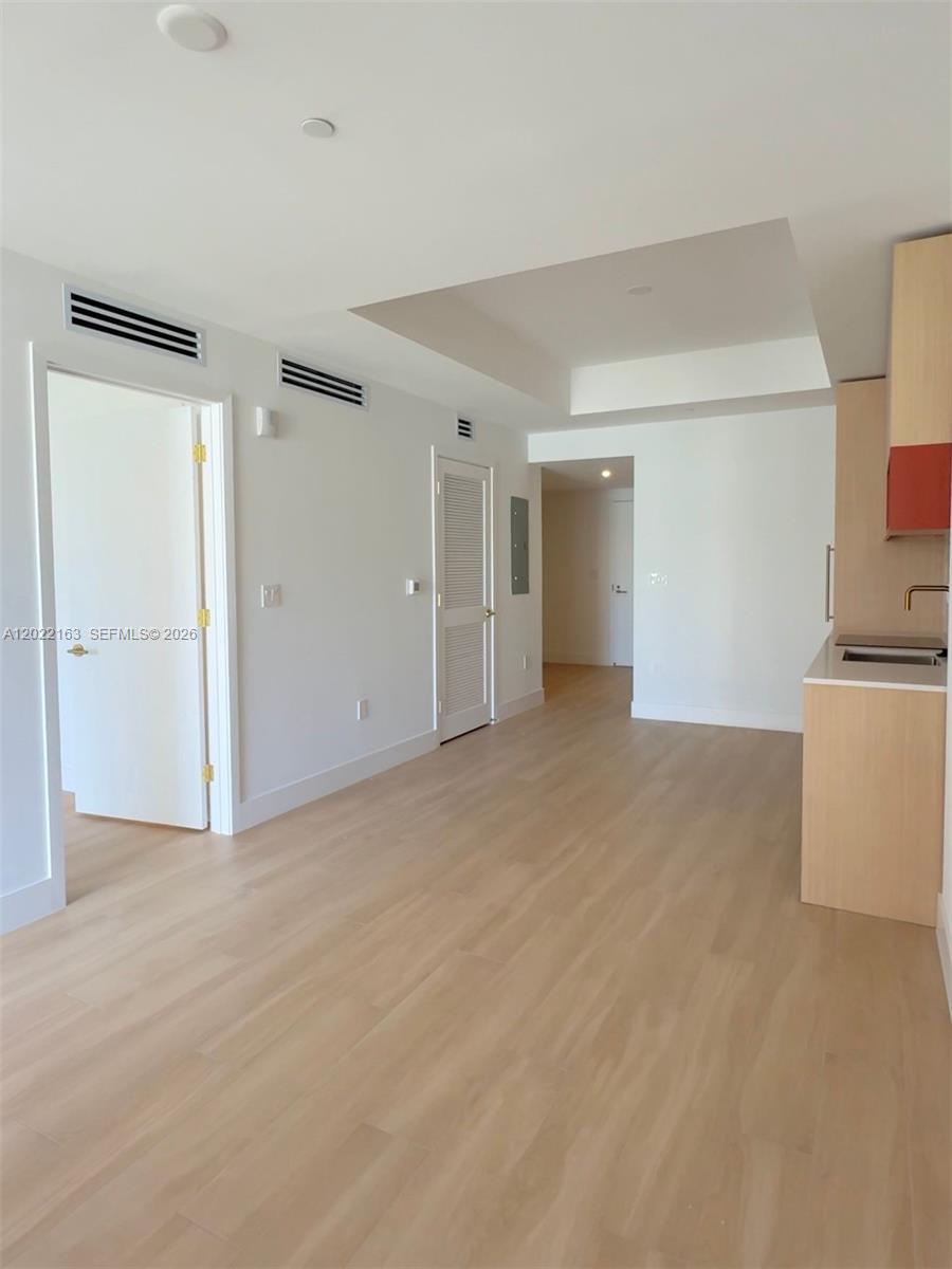 A bright, modern room features light wood flooring, white walls, and a minimalist kitchen area — 90 NE 32nd St # 510, Miami FL 33145, MIAMI, FL