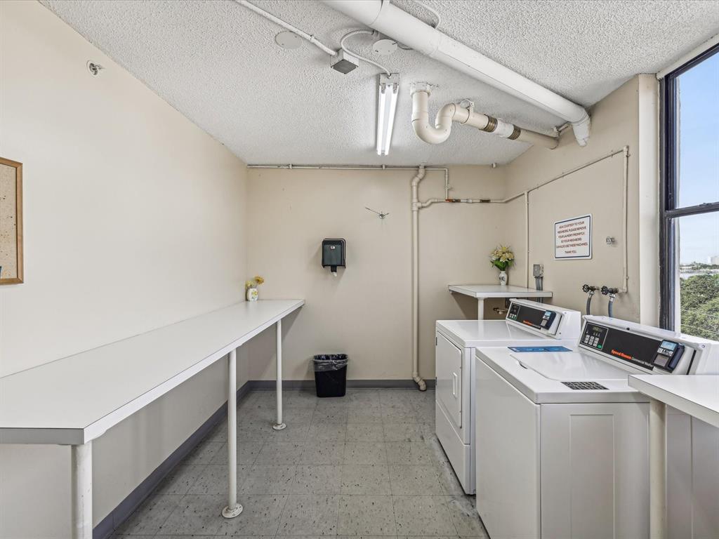 A laundry room features a long folding table, two washing machines, and exposed ceiling pipes — 255 DOLPHIN POINT UNIT 404, CLEARWATER BEACH, FL