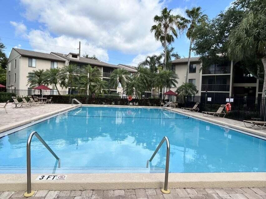 A rectangular swimming pool sits in front of a multi-story apartment building with palm trees — 203 Foxtail Drive # B3, FL 33415, FL