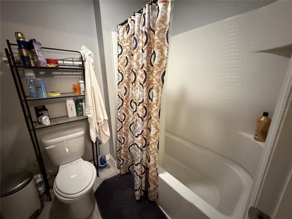 A bathroom features a toilet, a shower-tub combination with a patterned curtain, and metal shelving — 1874 HICKORY BLUFF ROAD, KISSIMMEE, FL
