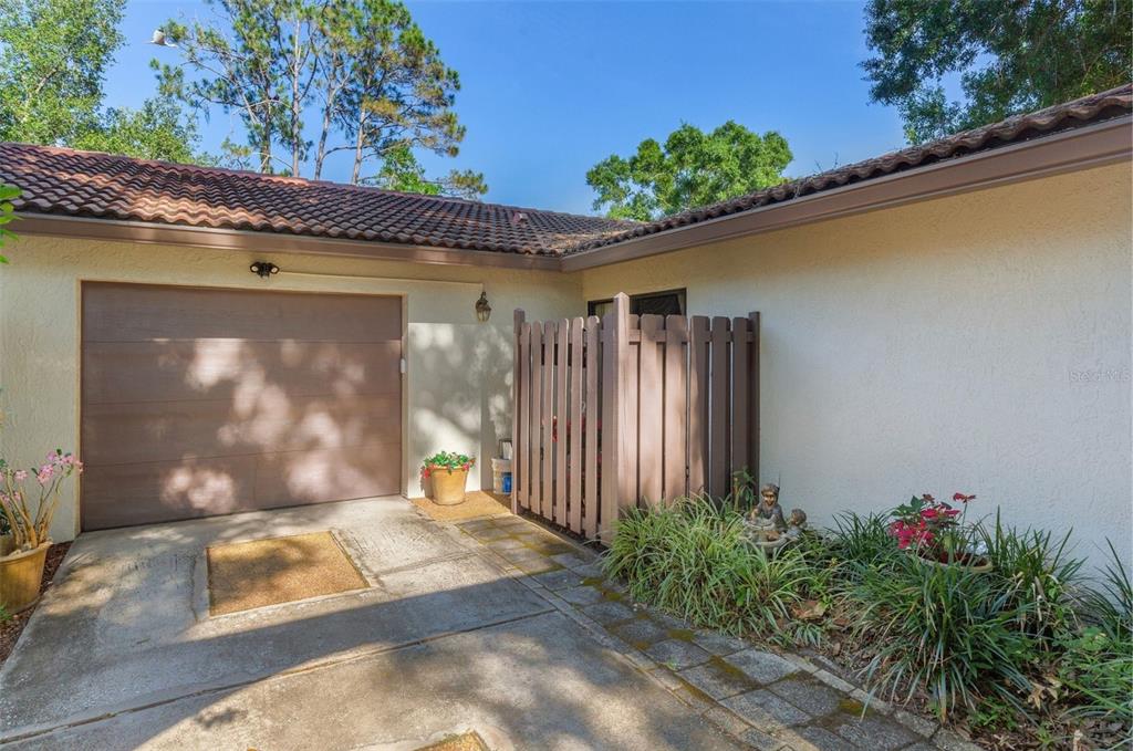 A residential exterior view shows a garage, a privacy fence, and a landscaped garden area — 3446 TARPON WOODS BOULEVARD, PALM HARBOR, FL