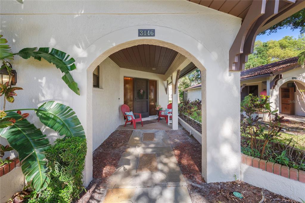 A covered entryway features a concrete walkway, two red chairs, and a front door — 3446 TARPON WOODS BOULEVARD, PALM HARBOR, FL
