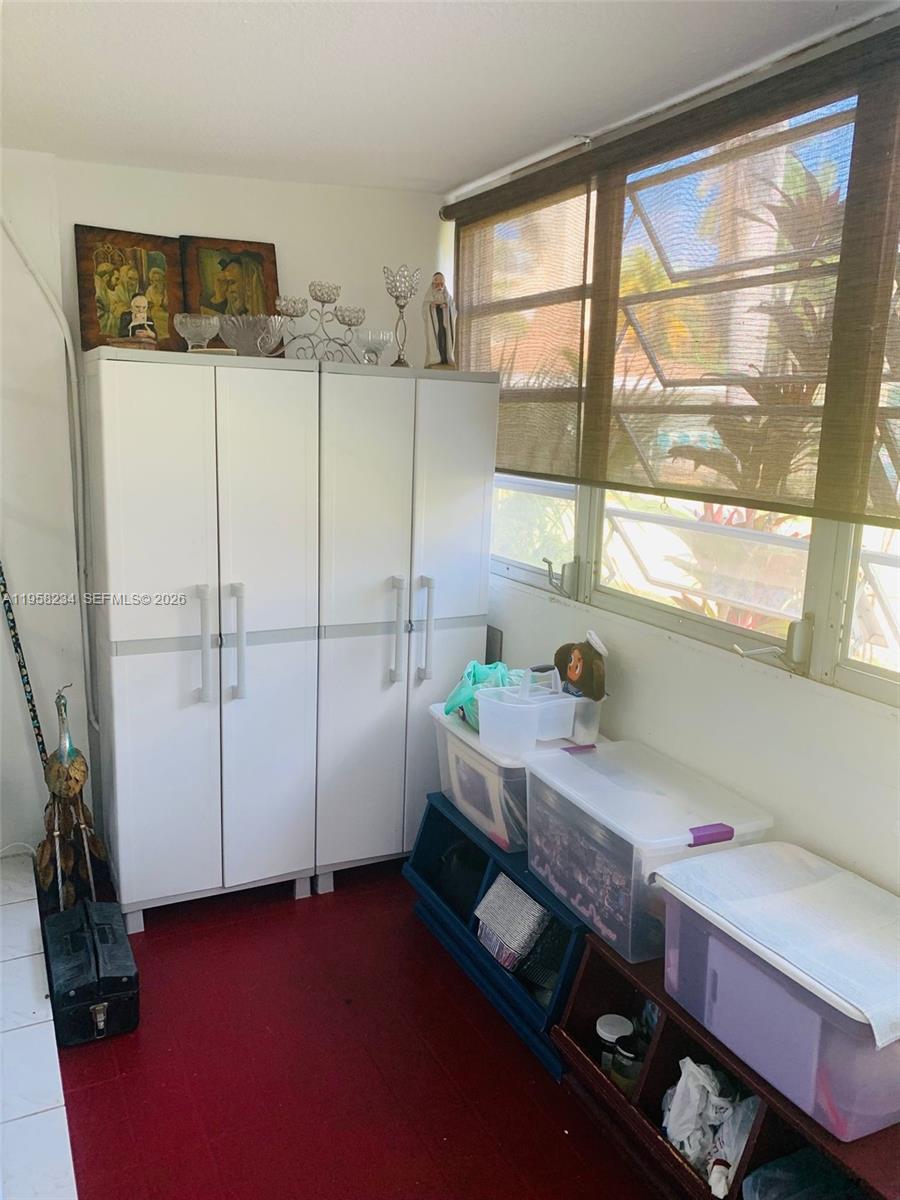 A sunroom features a white storage cabinet, plastic storage bins, and red flooring — 1333 HALLANDALE BEACH BL # 131, Hallandale Beach FL 33009, HALLANDALE BEACH, FL