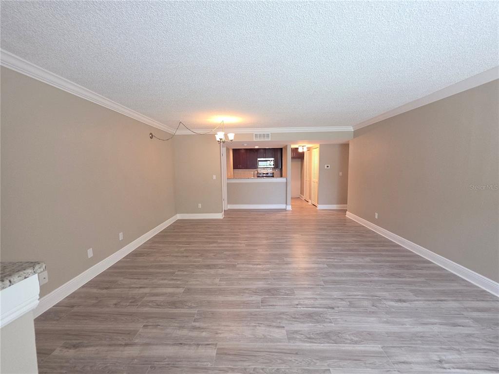 A spacious living area with light wood-look flooring leads to an open kitchen — 2599 COUNTRYSIDE BOULEVARD UNIT 117, CLEARWATER, FL