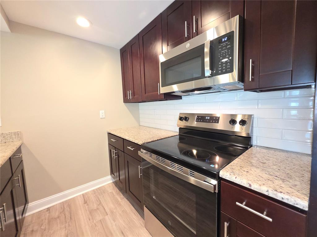 A kitchen featuring dark wood cabinets, granite countertops, stainless steel appliances, and a white backsplash — 2599 COUNTRYSIDE BOULEVARD UNIT 117, CLEARWATER, FL