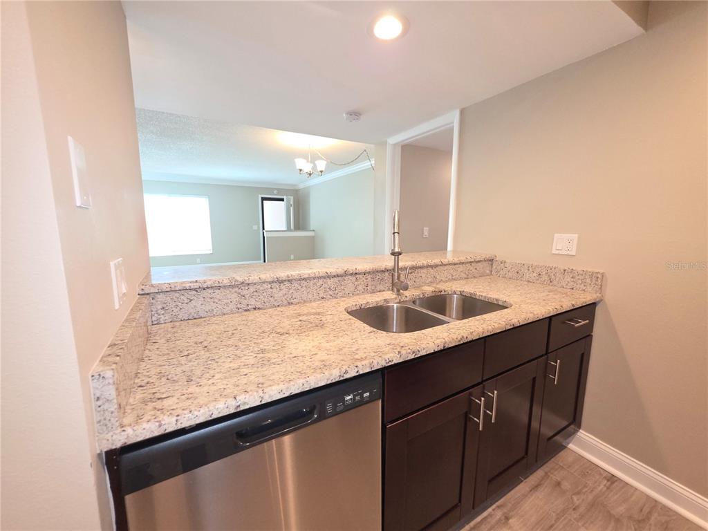 A kitchen features dark wood cabinets, granite countertops, a stainless steel dishwasher, and a sink — 2599 COUNTRYSIDE BOULEVARD UNIT 117, CLEARWATER, FL