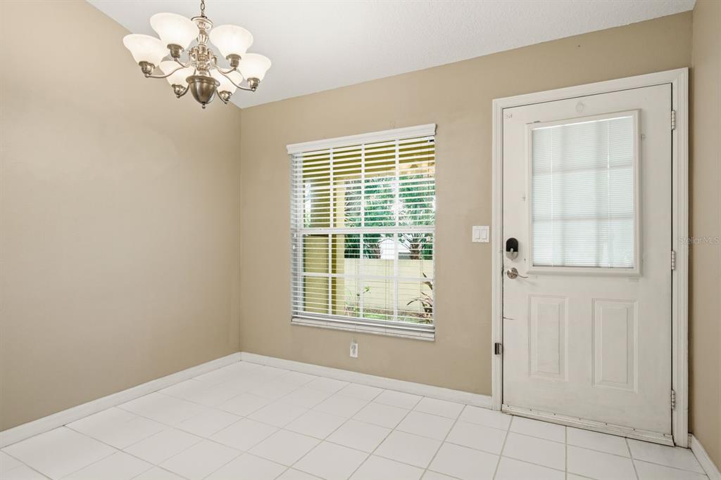 A dining area with white tile floors, a chandelier, a window with blinds, and a door — 406 S BAYVIEW BOULEVARD UNIT 1, OLDSMAR, FL