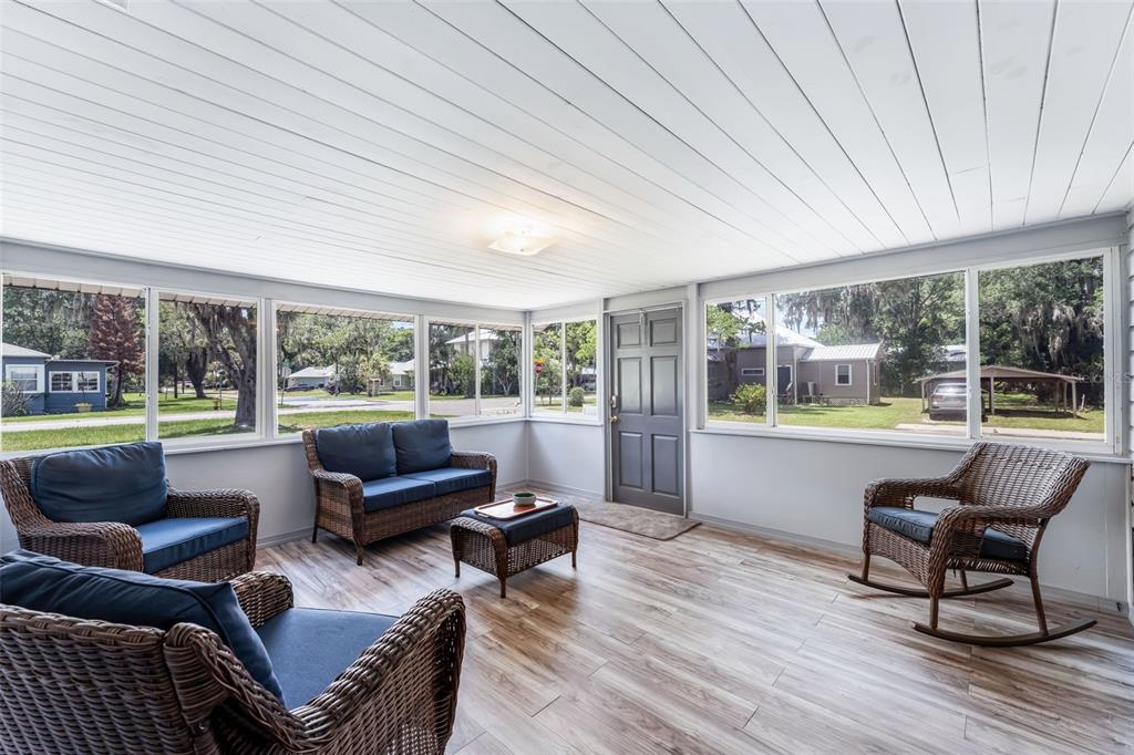 A sunroom features wicker furniture, wood-look flooring, a white paneled ceiling, and large windows — 302 PARK AVENUE, HASTINGS, FL