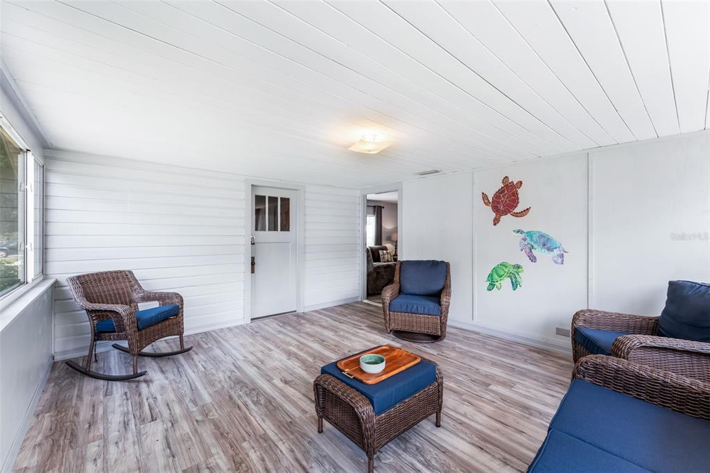 A sunroom features white paneled walls, wood-look flooring, wicker furniture, and turtle wall art — 302 PARK AVENUE, HASTINGS, FL