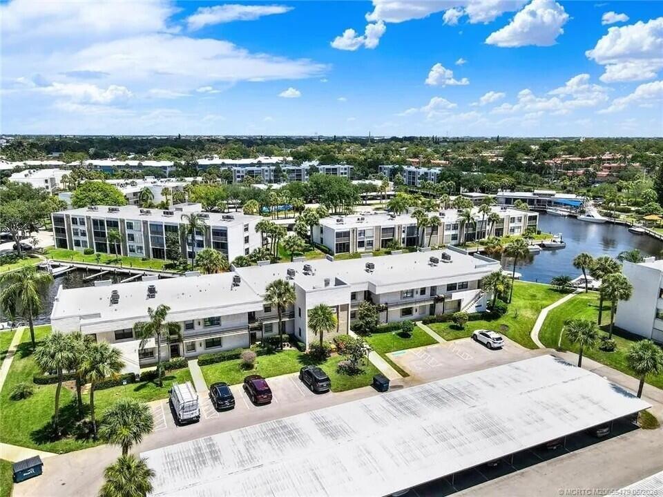 An aerial view shows multi-story apartment buildings with parking lots and a nearby canal — 1950 SW Palm City Road # 102, Stuart FL 34994, STUART, FL