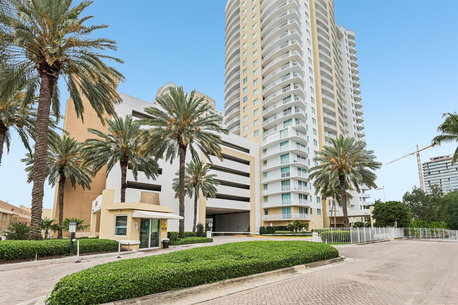 A tall residential high-rise building features a gated entrance, palm trees, and a parking garage — 1755 E Hallandale Beach Boulevard, Hallandale Beach FL 33009, HALLANDALE BEACH, FL