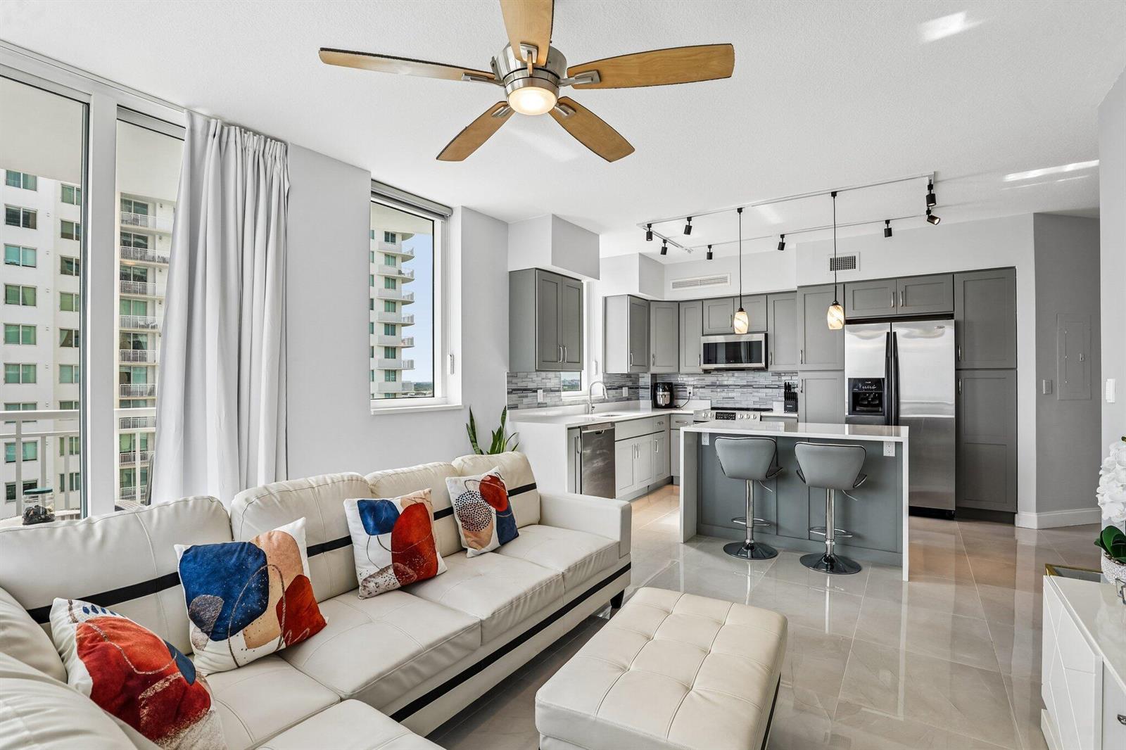 A modern open-concept apartment features a white sofa, kitchen island, and gray cabinetry — 1755 E Hallandale Beach Boulevard, Hallandale Beach FL 33009, HALLANDALE BEACH, FL