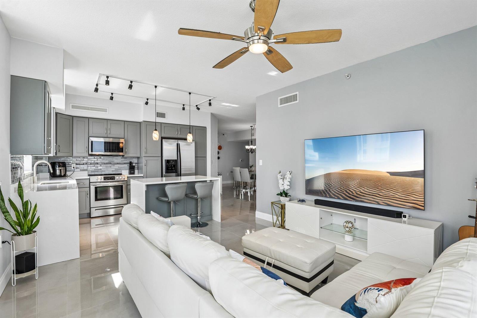 An open-concept living room and kitchen featuring grey cabinetry, white countertops, and a large television — 1755 E Hallandale Beach Boulevard, Hallandale Beach FL 33009, HALLANDALE BEACH, FL