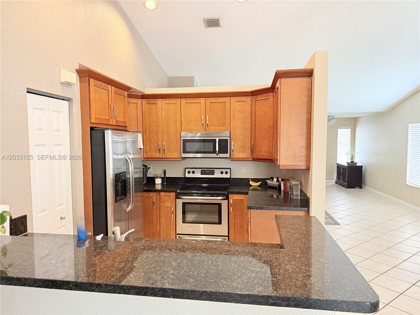A kitchen features wood cabinets, stainless steel appliances, and dark granite countertops — 1530 Canary Island Dr, Weston FL 33327, WESTON, FL