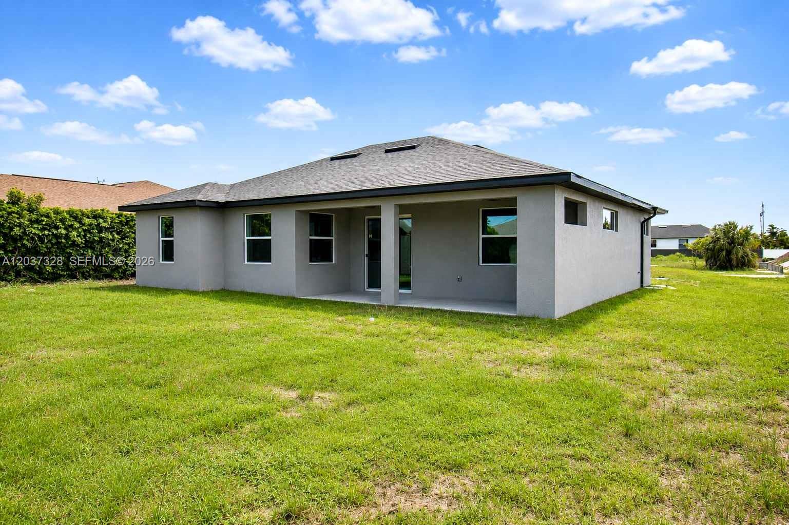 The rear exterior of a gray single-story house features a covered patio and lawn — 3909 16TH ST W, Lehigh Acres FL 33971, LEHIGH ACRES, FL