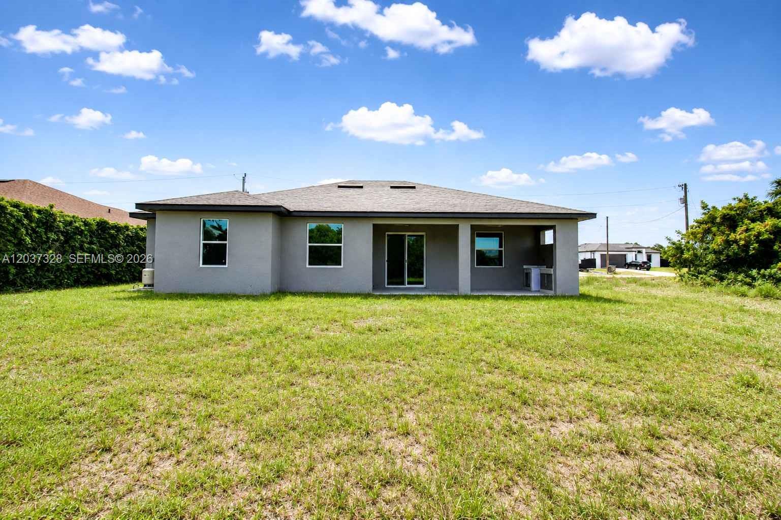The rear exterior of a gray single-story house features a covered patio and lawn — 3909 16TH ST W, Lehigh Acres FL 33971, LEHIGH ACRES, FL