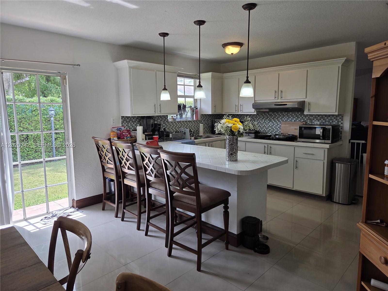 A backyard features a tiled patio with outdoor furniture, a grassy lawn, and tall hedges — 10120 SW 127th Ave, Miami FL 33186, MIAMI, FL