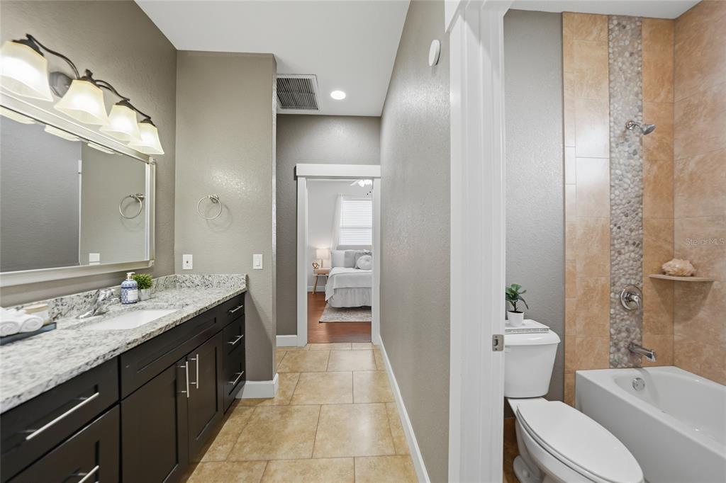 A bathroom features a dark vanity with granite countertops, a tiled tub-shower, and a doorway — 1480 WISE DRIVE, NORTH PORT, FL