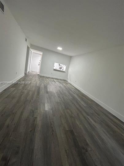 An empty room with gray wood-look flooring, white walls, and a small kitchen pass-through window — 8875 Fontainebleau Blvd # 201, Miami FL 33172, MIAMI, FL