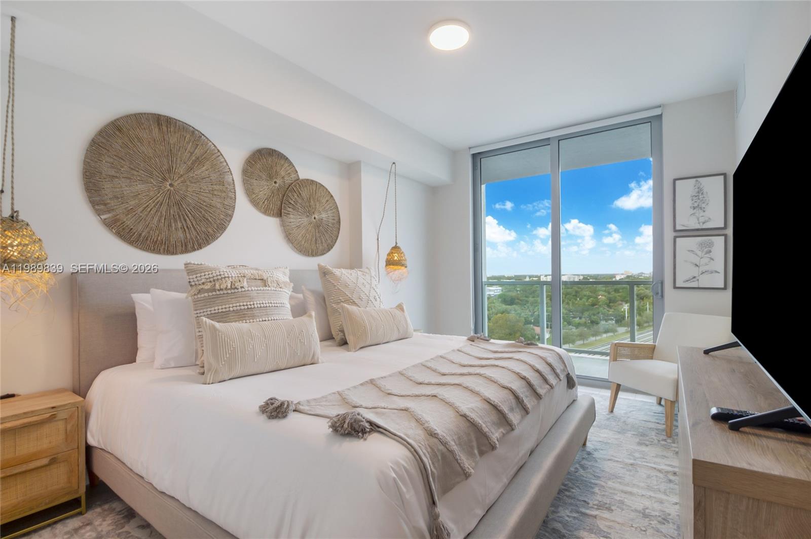 A bedroom features a bed with textured pillows, wall-mounted decor, and a balcony with views — 3900 Biscayne Blvd # 911, Miami FL 33137, MIAMI, FL