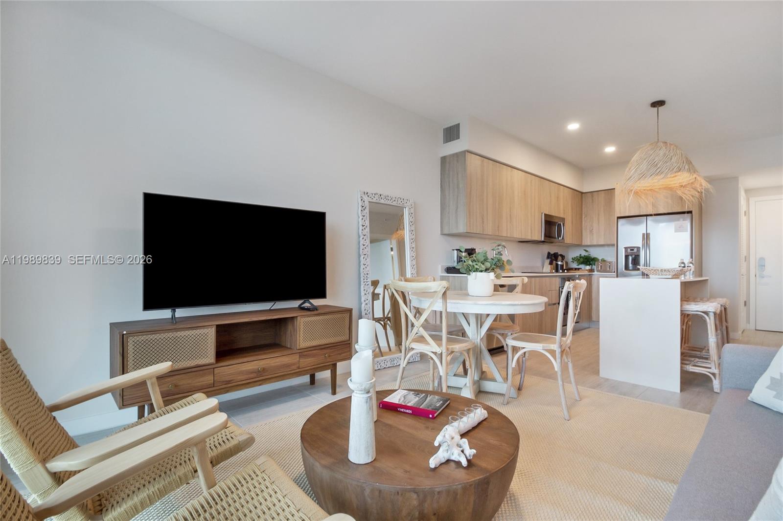 A living room and kitchen area feature light wood cabinetry, a round table, and rattan furniture — 3900 Biscayne Blvd # 911, Miami FL 33137, MIAMI, FL