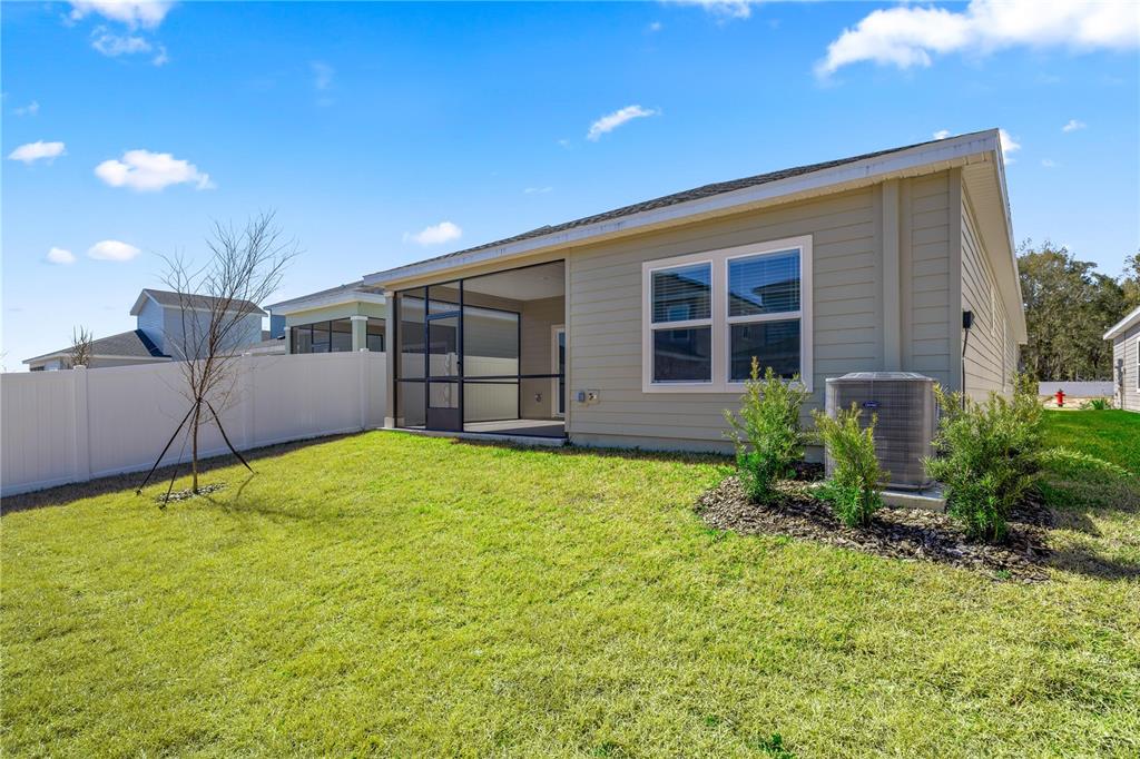 The exterior of a beige house features a screened-in porch, a grassy yard, and fencing — 8704 SW 67TH CIRCLE, OCALA, FL