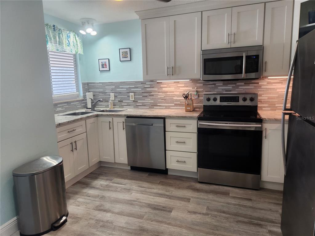 A kitchen features white cabinets, stainless steel appliances, a tiled backsplash, and wood-look flooring — 1008 APOLLO BEACH BOULEVARD UNIT 204, APOLLO BEACH, FL
