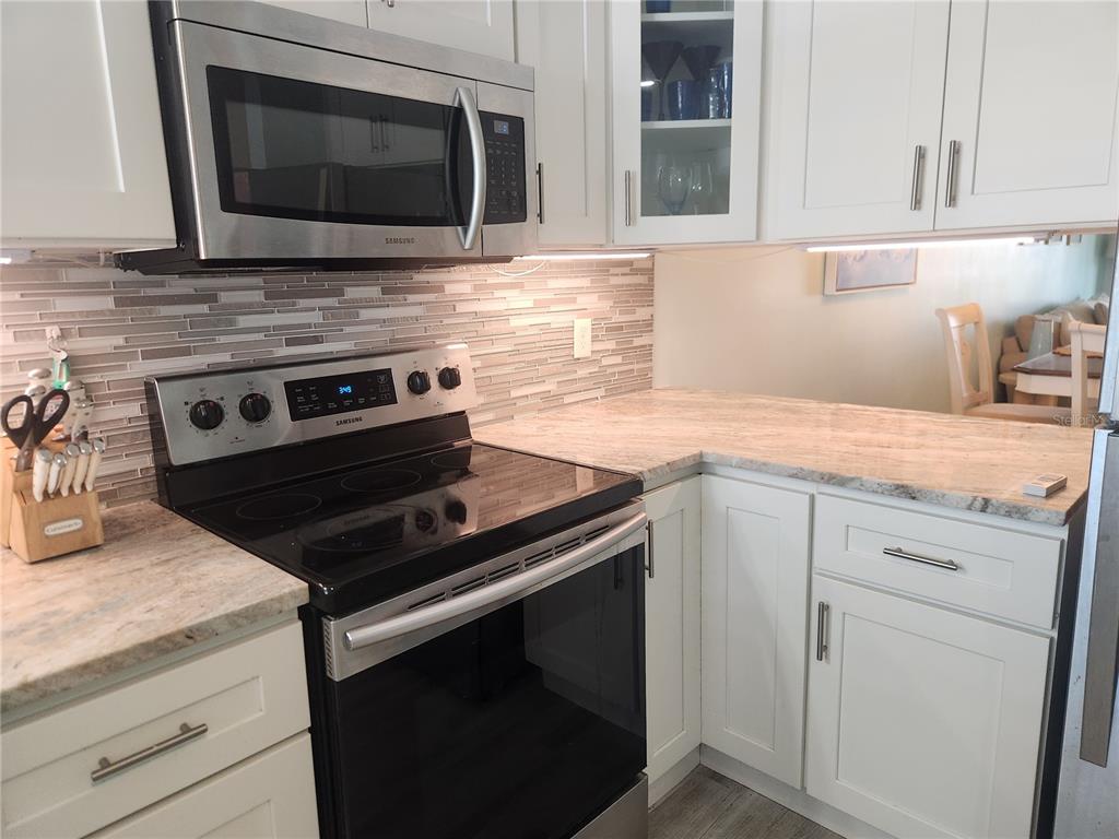 A kitchen features white cabinets, a stainless steel stove and microwave, and a tiled backsplash — 1008 APOLLO BEACH BOULEVARD UNIT 204, APOLLO BEACH, FL