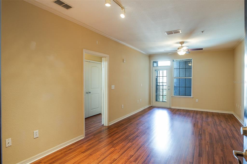 An empty living room features tan walls, wood-look flooring, a ceiling fan, and a glass door — 4221 W SPRUCE STREET UNIT 1310, TAMPA, FL
