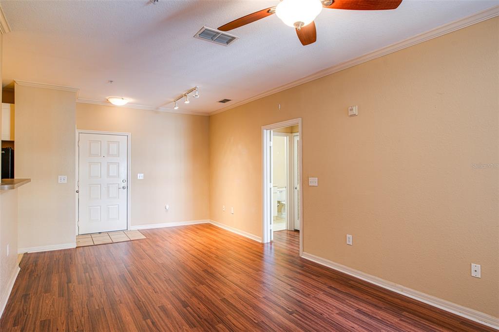 An empty living room features wood-look flooring, tan walls, a ceiling fan, and an entryway — 4221 W SPRUCE STREET UNIT 1310, TAMPA, FL