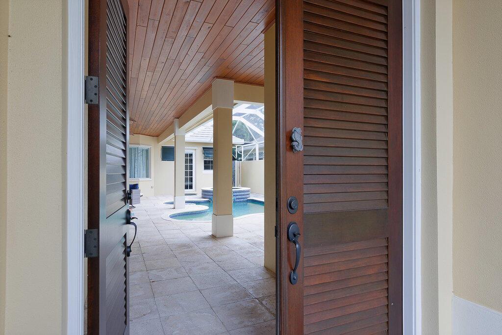 A view through an open louvered door reveals a covered patio with a swimming pool — 9190 Spring Time Drive, Vero Beach FL 32963, VERO BEACH, FL