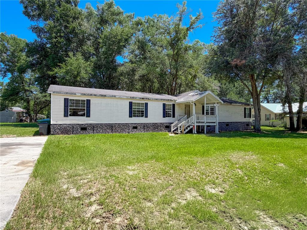 A single-story manufactured home with light siding, dark shutters, and a front porch — 303 NW KENSINGTON LANE, LAKE CITY, FL