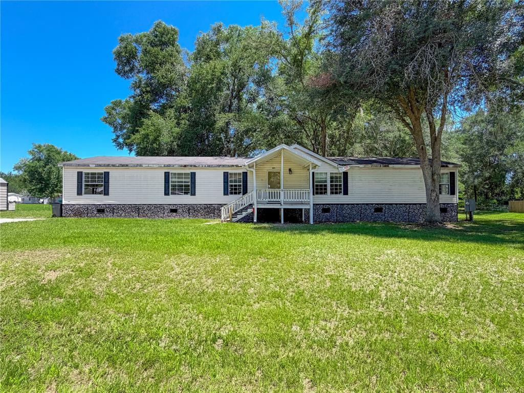 A single-story manufactured home with light siding and a stone-patterned foundation sits on grass — 303 NW KENSINGTON LANE, LAKE CITY, FL