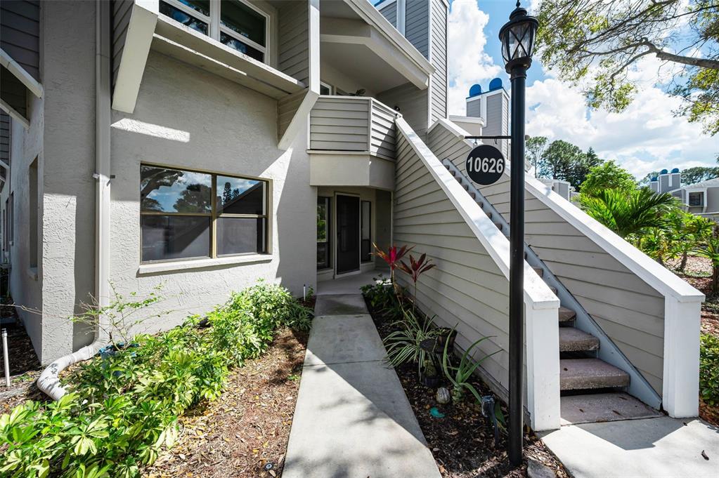 A concrete walkway leads to the entrance of a multi-story building with gray siding — 10626 LONGWOOD DRIVE UNIT 102, SEMINOLE, FL