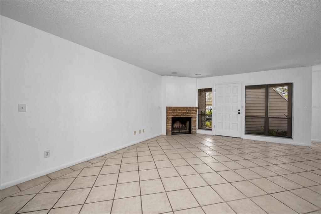 An empty living room features white walls, beige tile flooring, and a corner brick fireplace — 10626 LONGWOOD DRIVE UNIT 102, SEMINOLE, FL