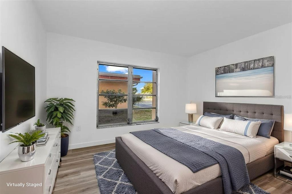 A bedroom with a gray upholstered bed, white dresser, and a window overlooking a yard — 2290 AARON STREET UNIT 109, PORT CHARLOTTE, FL