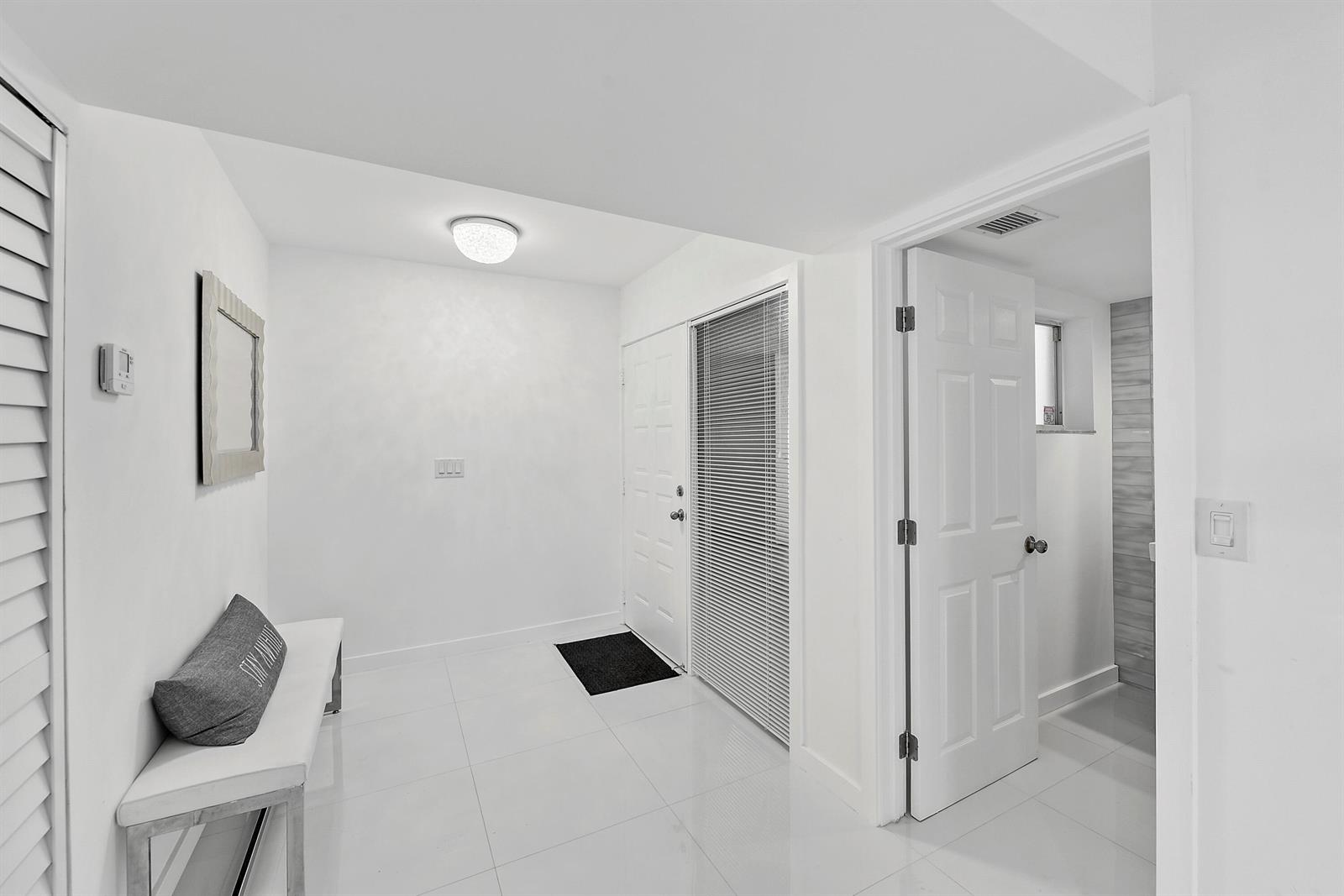A bright entryway features white tile floors, a bench, and a door leading to a bathroom — 7369 Orangewood Lane # 303, Boca Raton FL 33433, BOCA RATON, FL