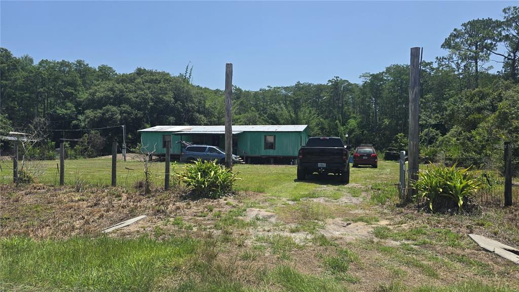 A green mobile home sits on a grassy lot behind a wire fence and gate — 135 STARLIGHT ROAD, CRESCENT CITY, FL