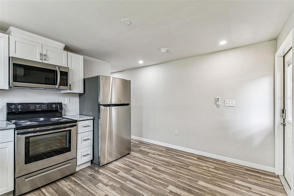 A kitchen with stainless steel appliances, white cabinets, and wood-look flooring — 1006 E 26TH AVENUE UNIT 1, TAMPA, FL
