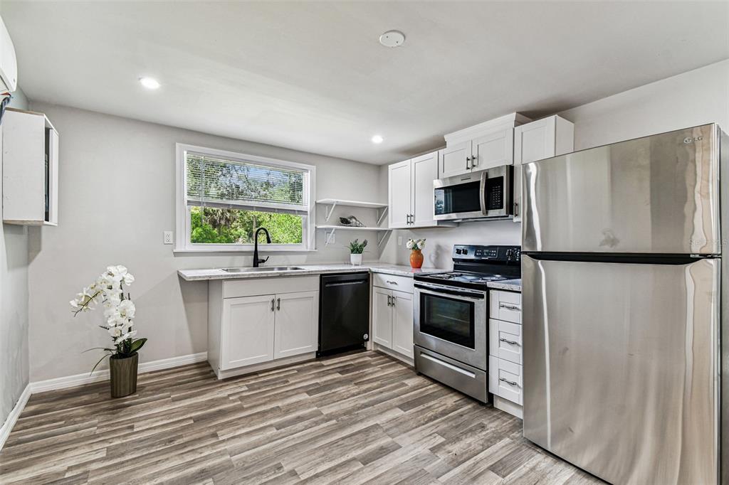 A kitchen features white cabinets, stainless steel appliances, a window above the sink, and wood-look flooring — 1006 E 26TH AVENUE UNIT 1, TAMPA, FL